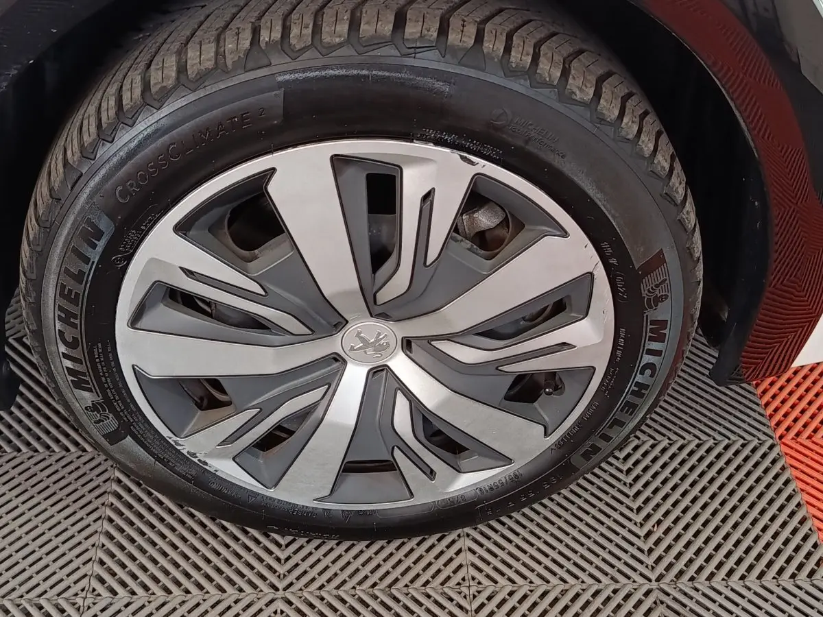 Gros plan sur la roue avant droite d’une Peugeot 208 électrique blanche, jante alliage au design moderne.