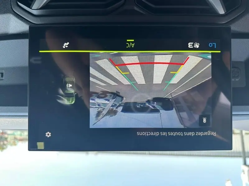 Écran tactile affichant la caméra de recul du Dacia Duster blanc, vue arrière avec lignes de guidage colorées.