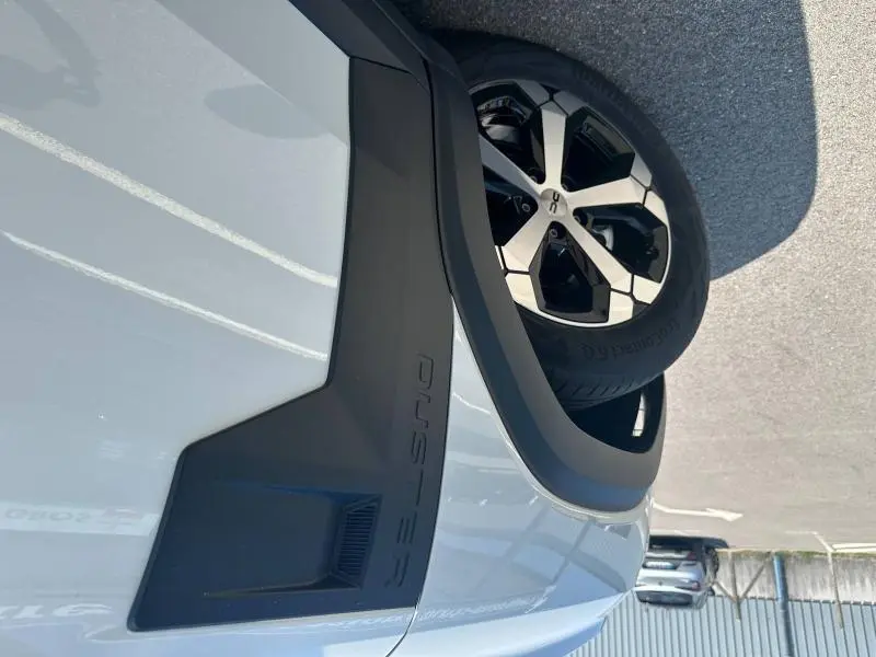 Gros plan sur l'aile avant droite blanche du Dacia Duster 2025 avec jante alu bicolore et logo Duster en relief.