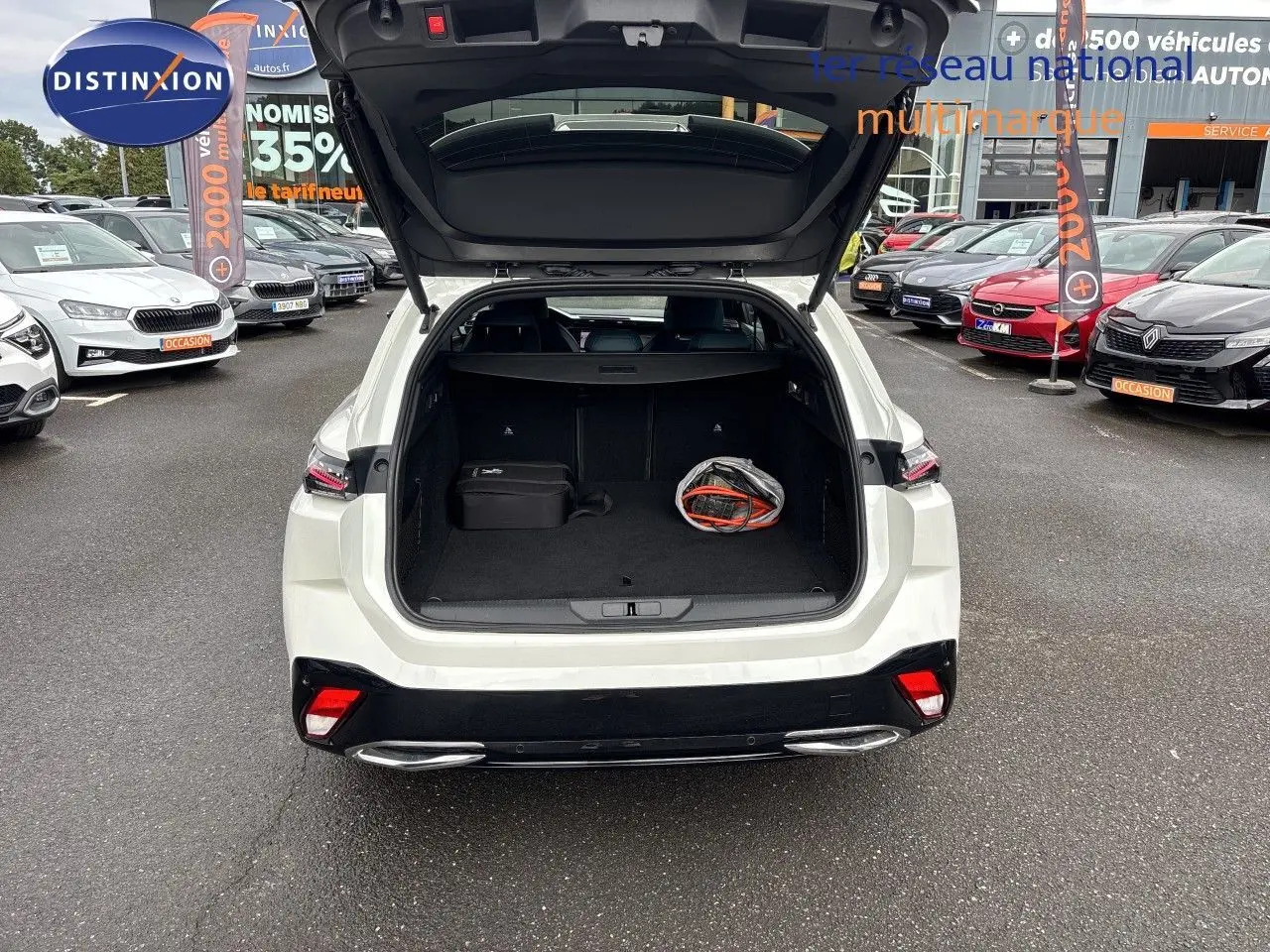 Vue arrière ouverte sur le coffre d'une Peugeot 308 SW hybride blanc nacré métal, avec un sac et une valise à l'intérieur.