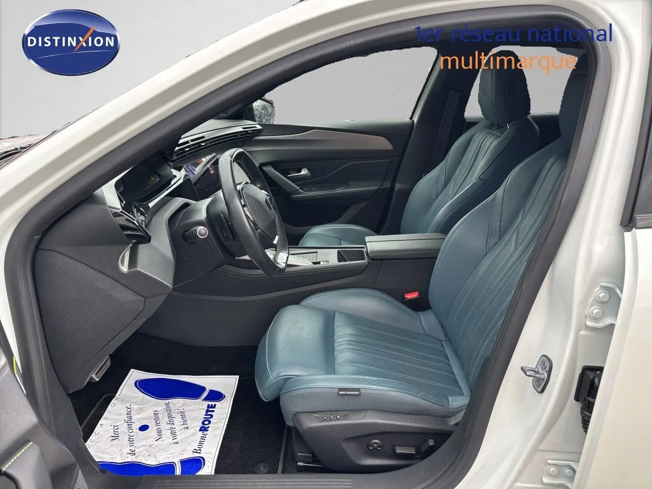 Intérieur côté conducteur de la Peugeot 308 SW hybride blanc nacré, sièges cuir bleu et tableau de bord moderne.