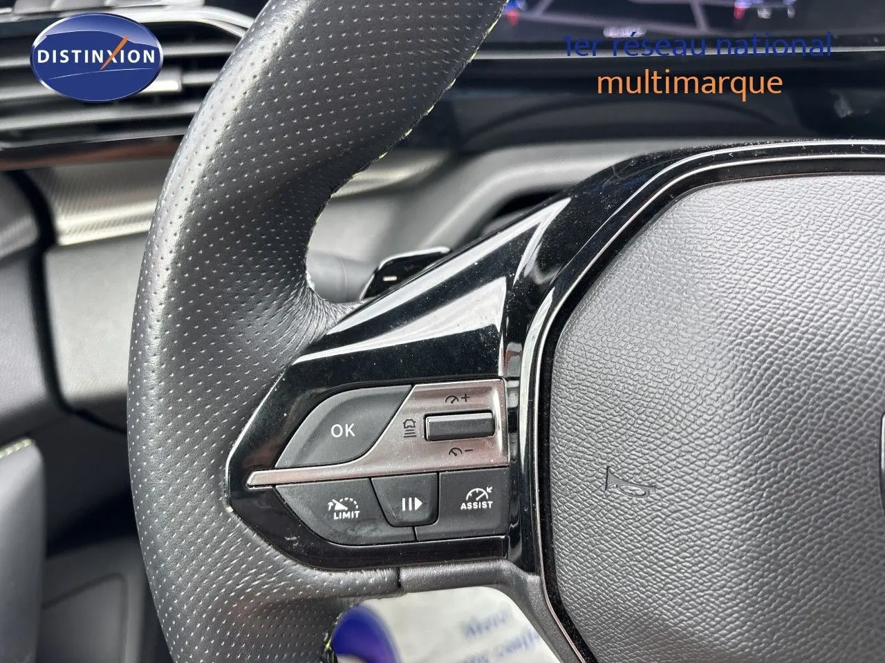 Gros plan sur le volant en cuir perforé côté gauche du Peugeot 308 SW blanc nacré, avec commandes intégrées.