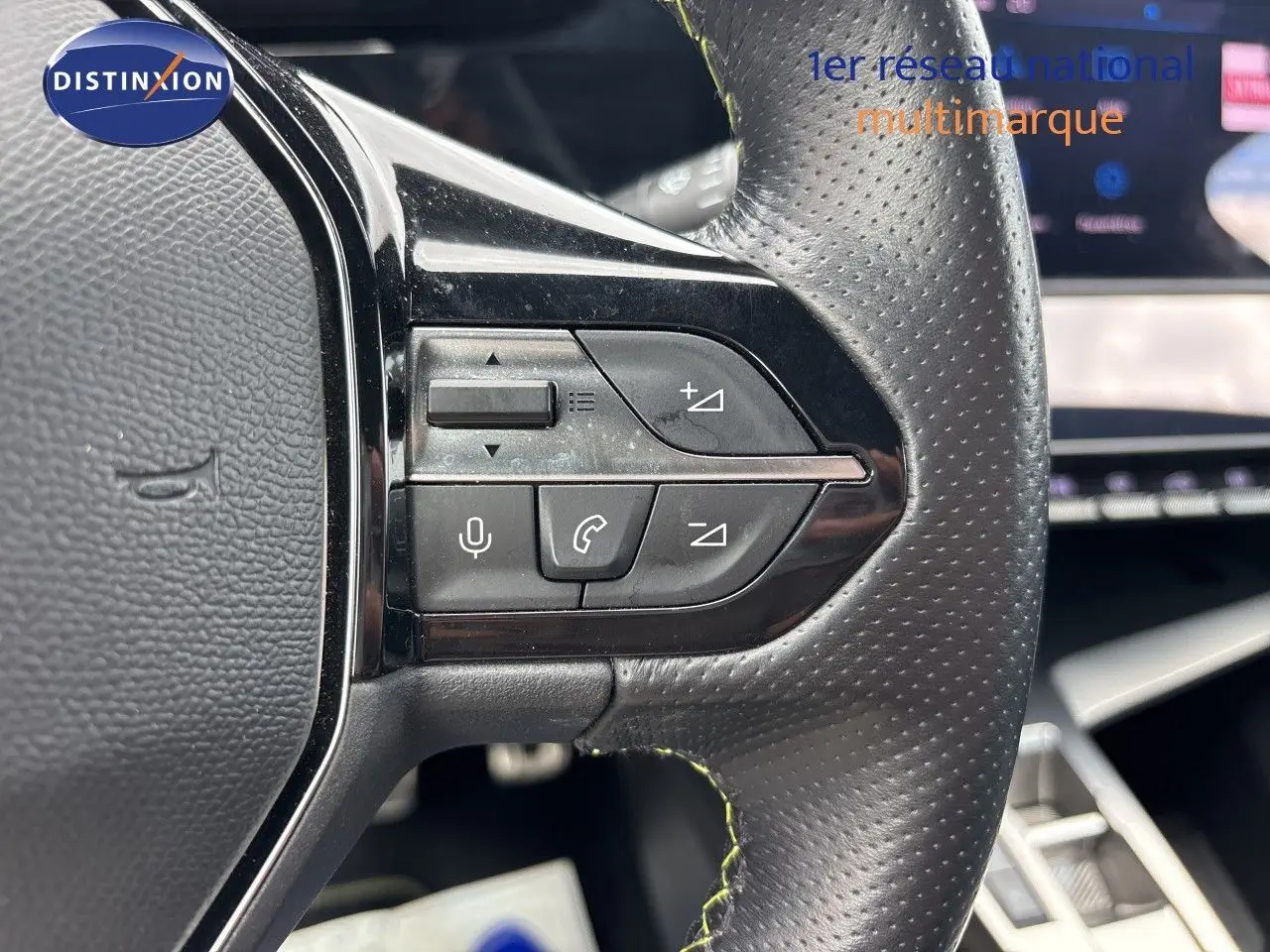 Gros plan sur les commandes au volant en cuir perforé noir du Peugeot 308 SW hybride, avec tableau de bord flou en arrière-plan.