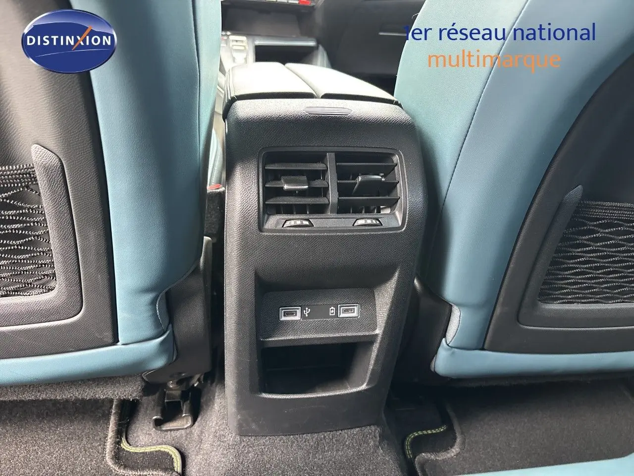 Vue rapprochée de la console arrière entre les sièges bleu clair d’un Peugeot 308 SW hybride blanc nacré, avec prises USB visibles.