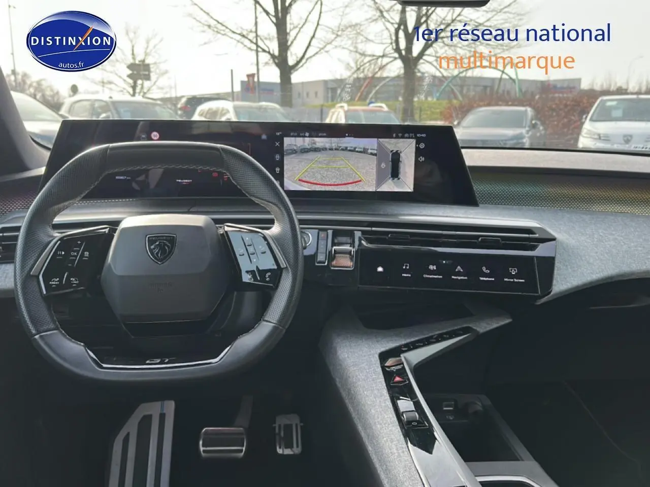 Vue intérieure frontale du tableau de bord et volant cuir noir du Peugeot 3008 gris Artense, avec écran tactile et caméra de recul affichée.