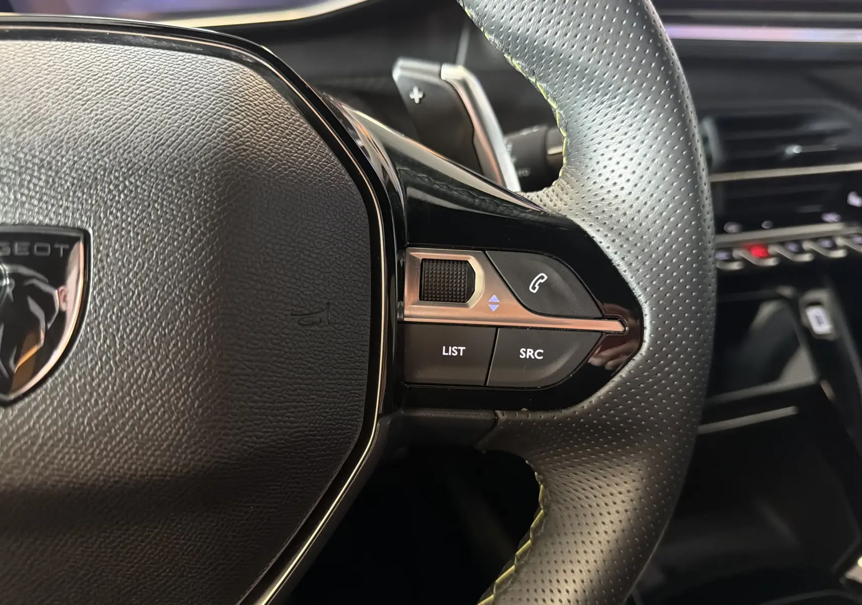 Gros plan sur le côté droit du volant perforé noir de la Peugeot 208 Hybrid 145 GT avec commandes intégrées.