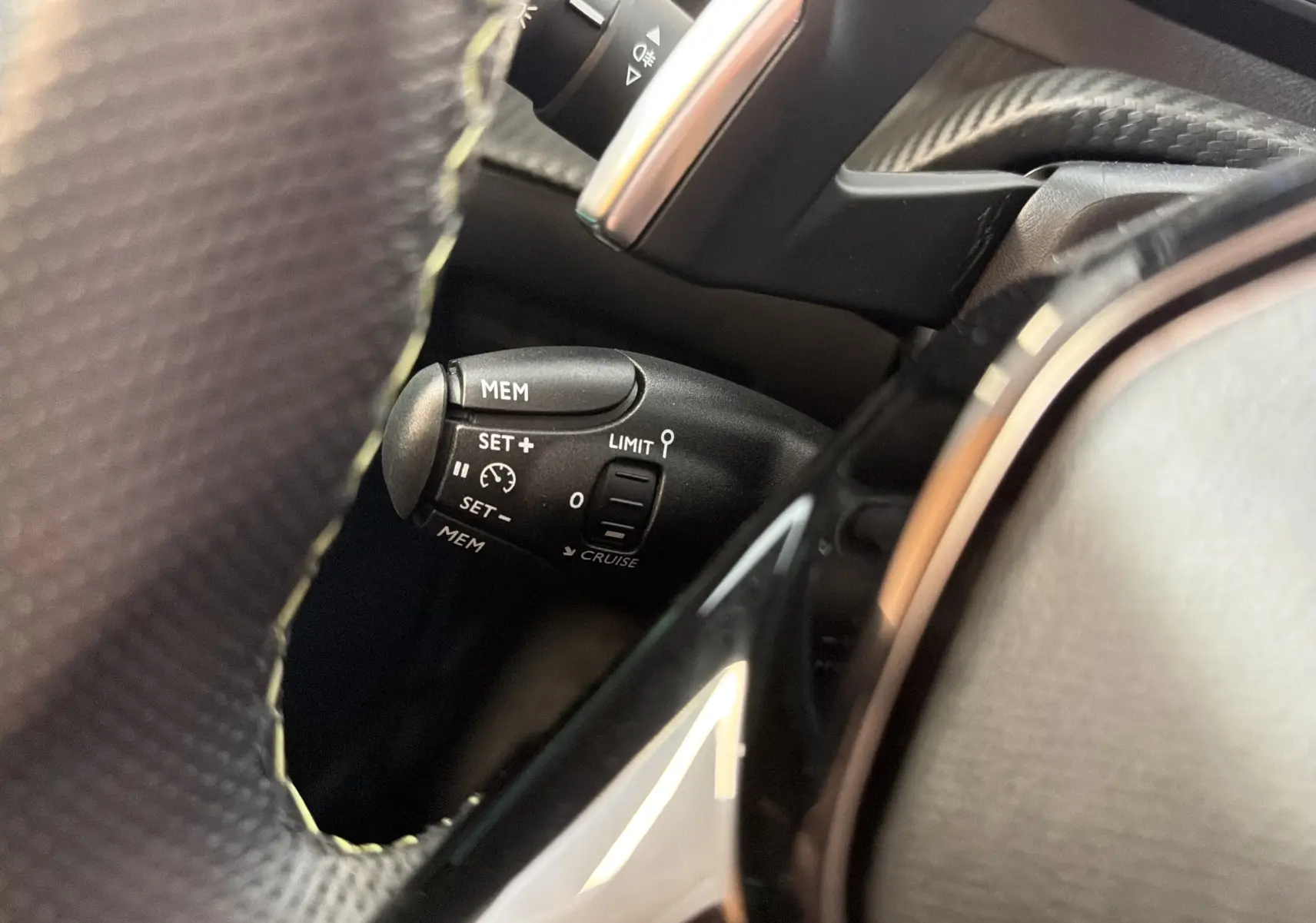 Gros plan sur la commande de régulateur de vitesse à gauche du volant d’une Peugeot 208 Hybrid 145 GT noir Perla.