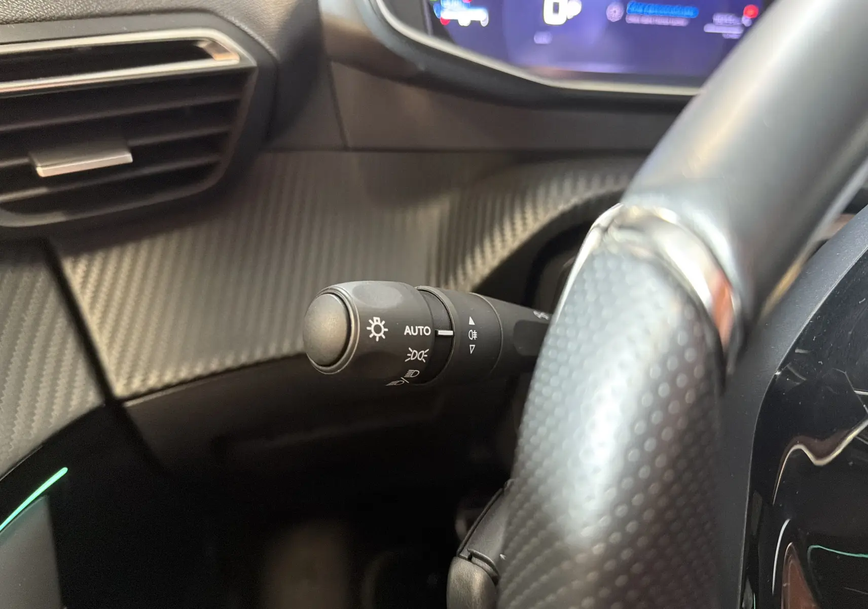 Gros plan sur la commande des feux au volant d’une Peugeot 208 Hybrid 145 GT, intérieur noir avec finition carbone.