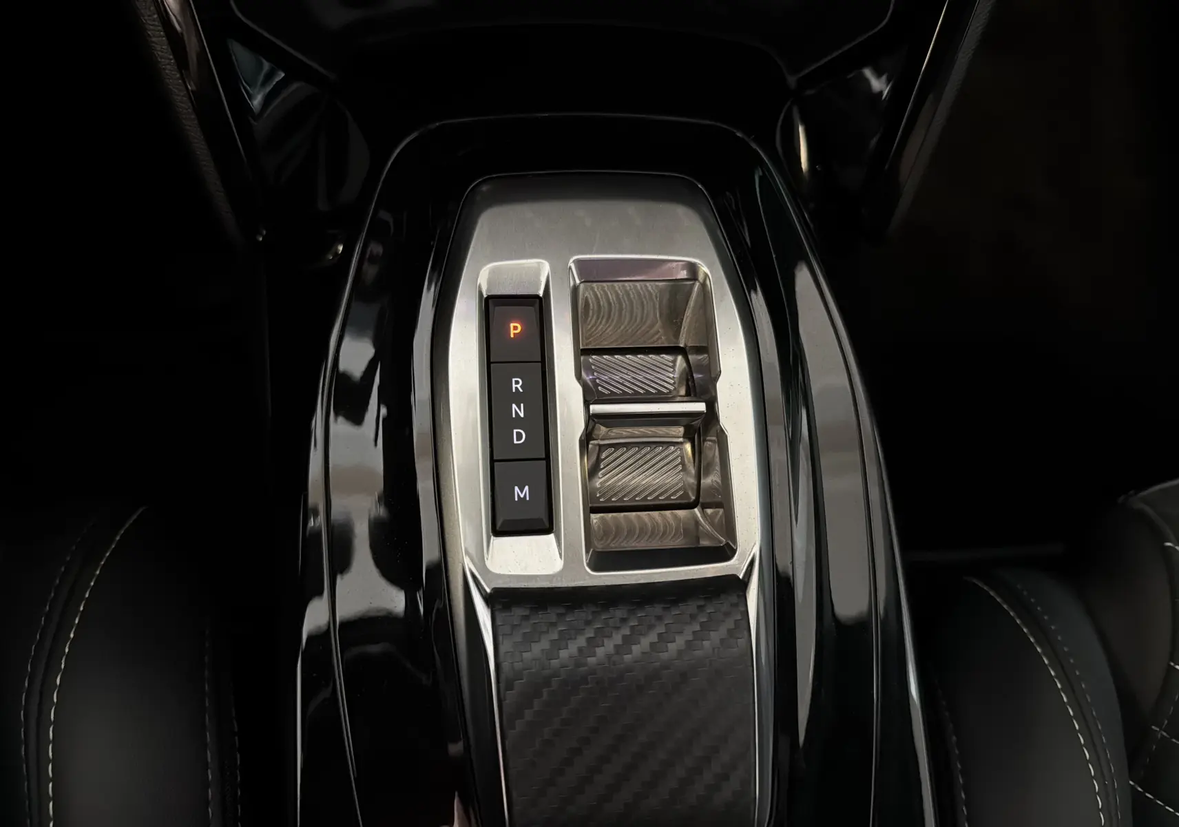 Gros plan sur la console centrale noire brillante de la Peugeot 208 HYBRID 145 e-DCS6 GT avec levier de vitesses électronique.