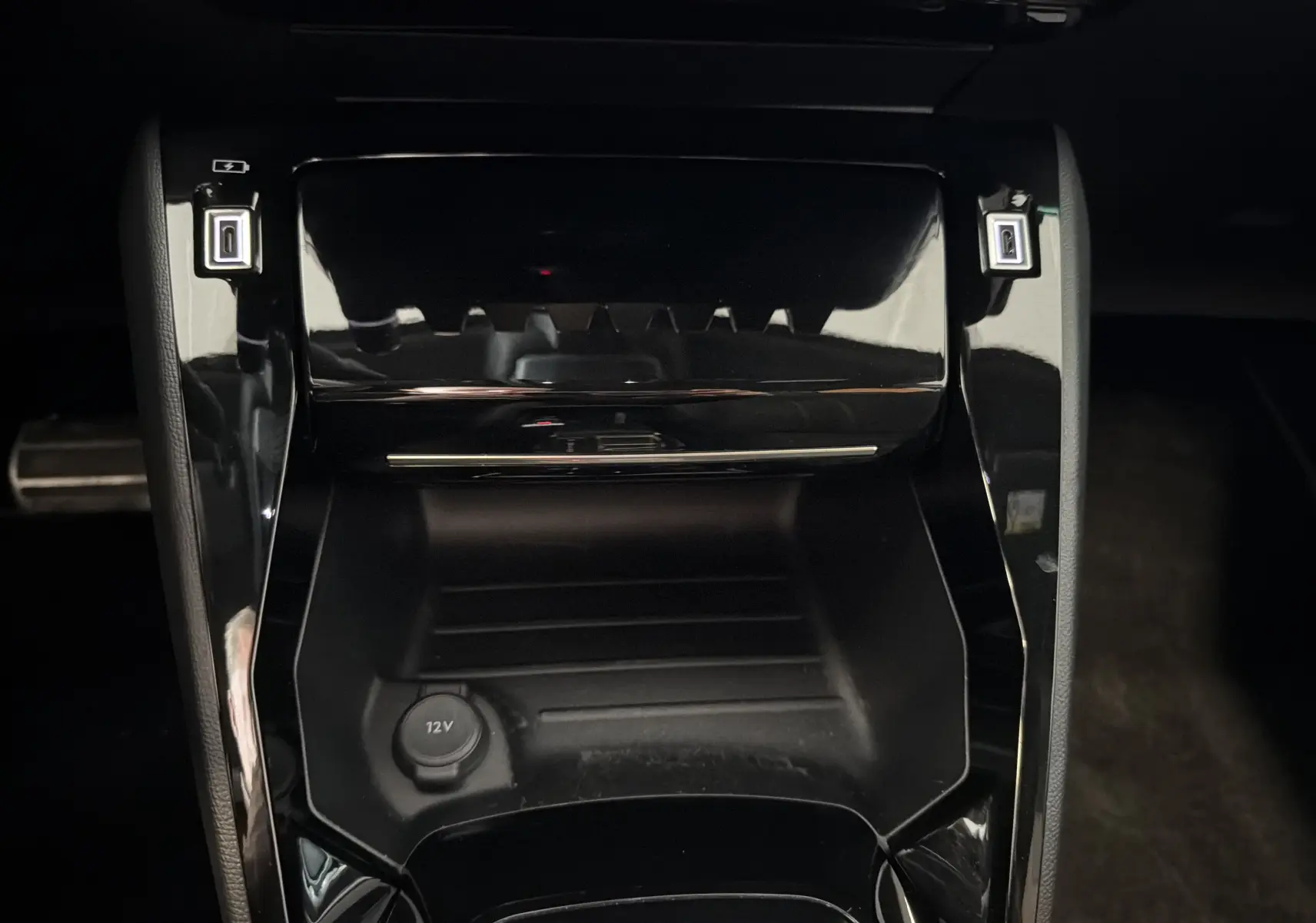 Gros plan sur la console centrale noire brillante de la Peugeot 208 Hybrid 145 e-DCS6 GT avec prise 12V et ports USB.