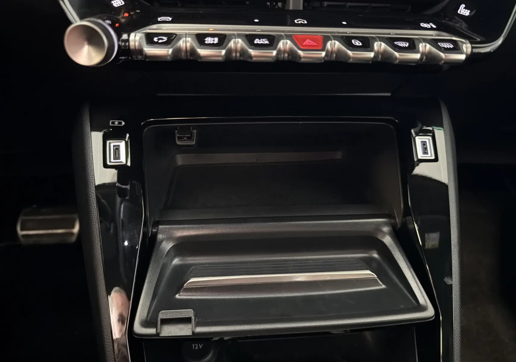 Vue rapprochée de la console centrale noire brillante du Peugeot 208 Hybrid 145 GT, avec commandes tactiles et rangement ouvert.
