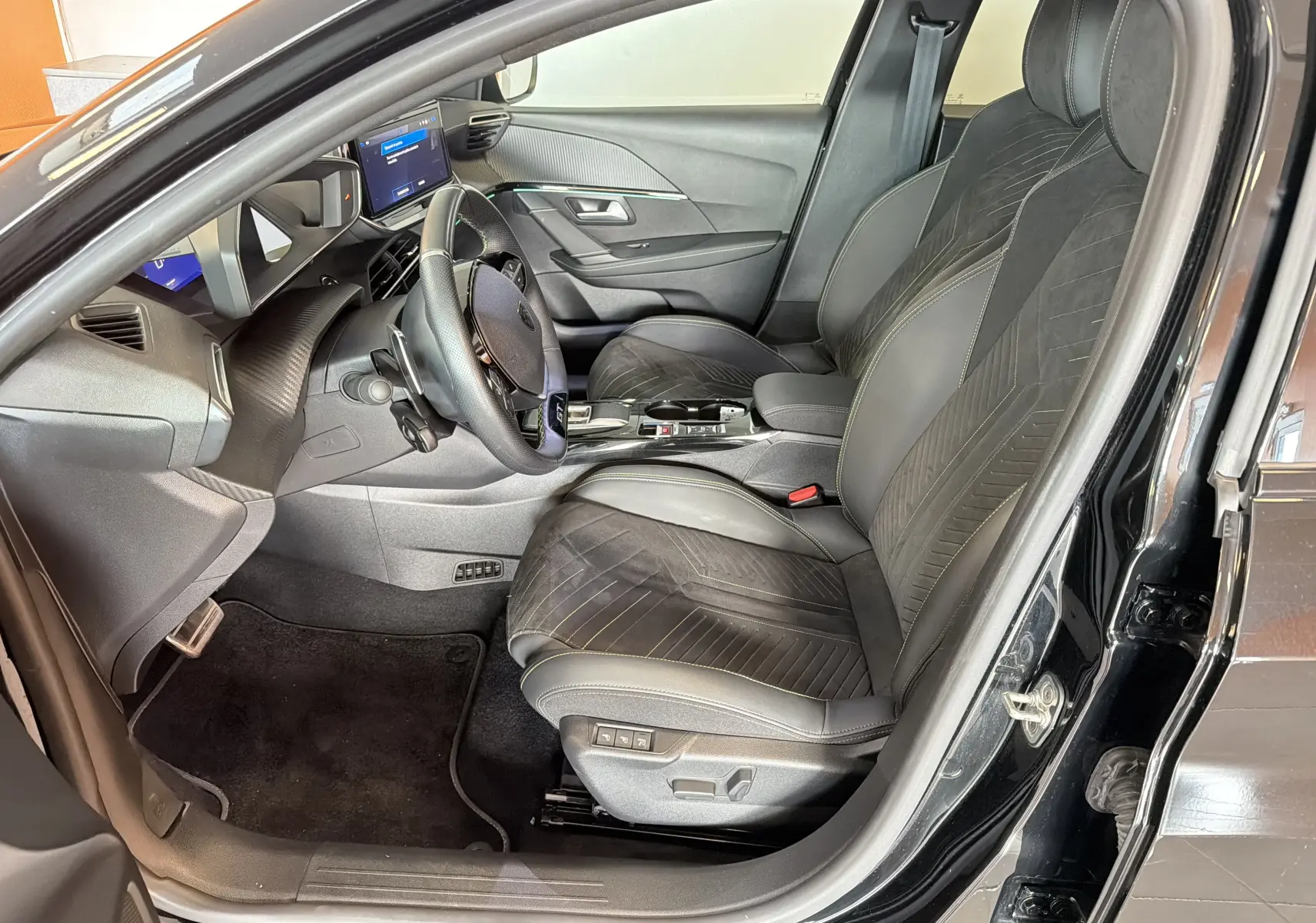 Intérieur avant droit de la Peugeot 208 Hybrid 145 GT 2025, sièges Alcantara noir avec surpiqûres vertes et tableau de bord moderne.