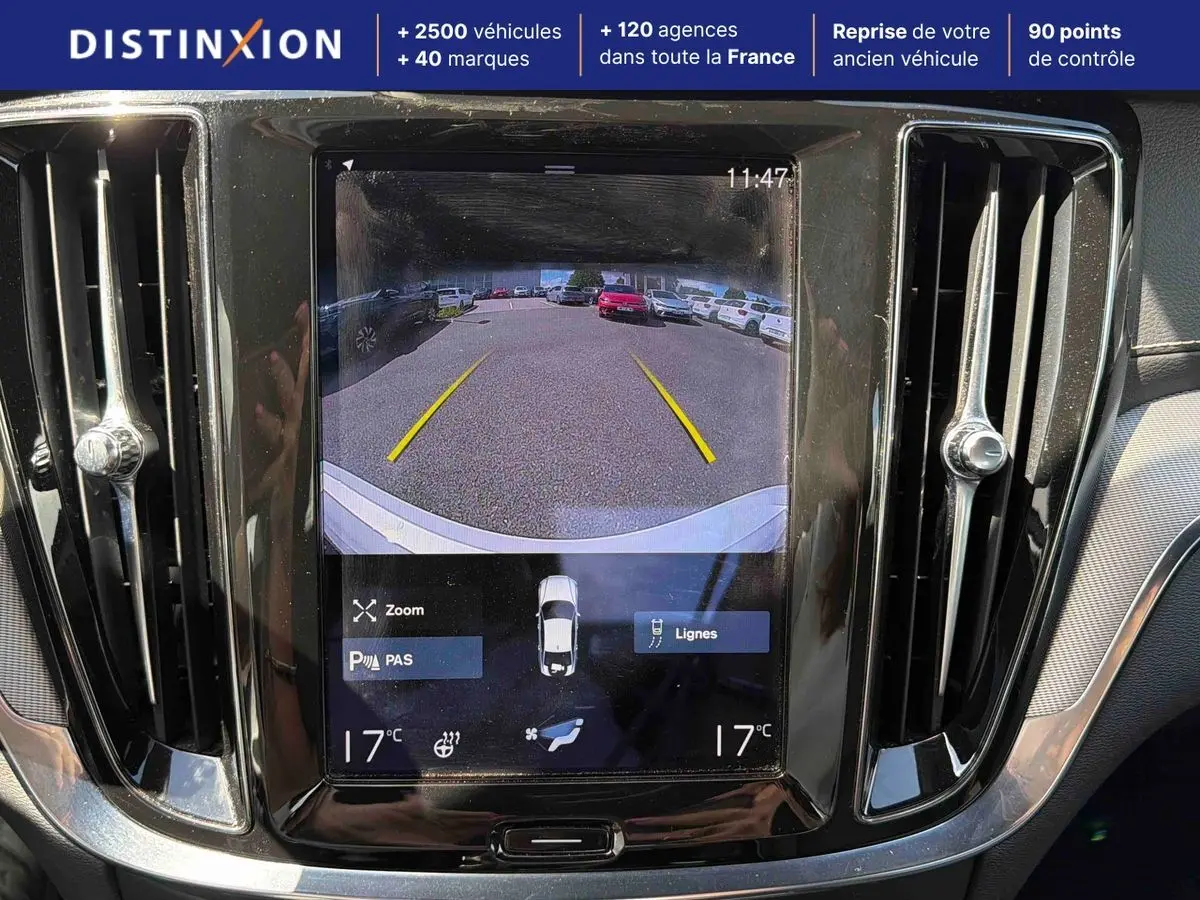Écran central tactile montrant la caméra de recul d'une Volvo S60 blanche, avec aérateurs latéraux chromés.