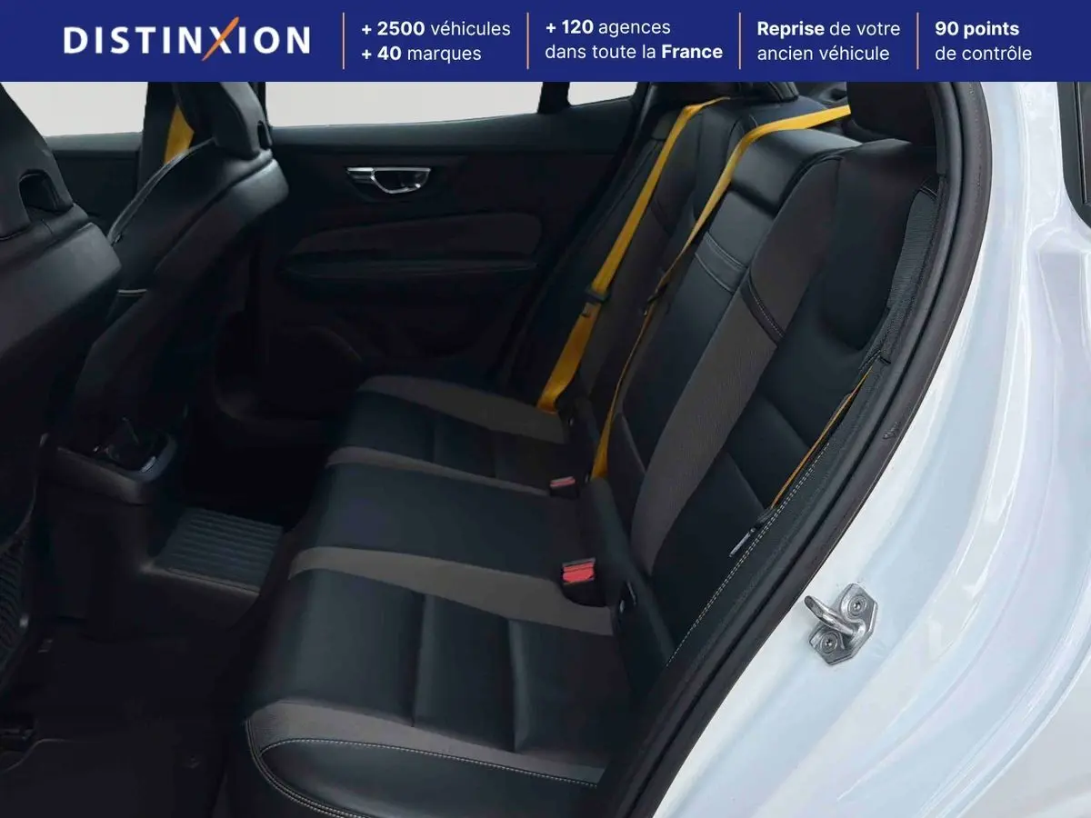 Vue intérieure côté arrière droit d'une Volvo S60 blanche, sièges arrière en cuir noir avec ceintures jaunes dorées.