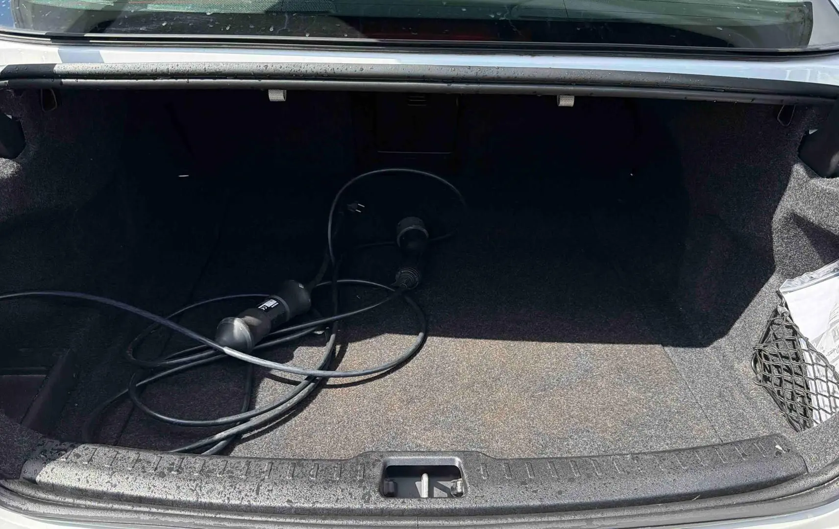 Coffre ouvert d'une Volvo S60 blanche de 2021 avec câble de recharge électrique visible à l'intérieur.