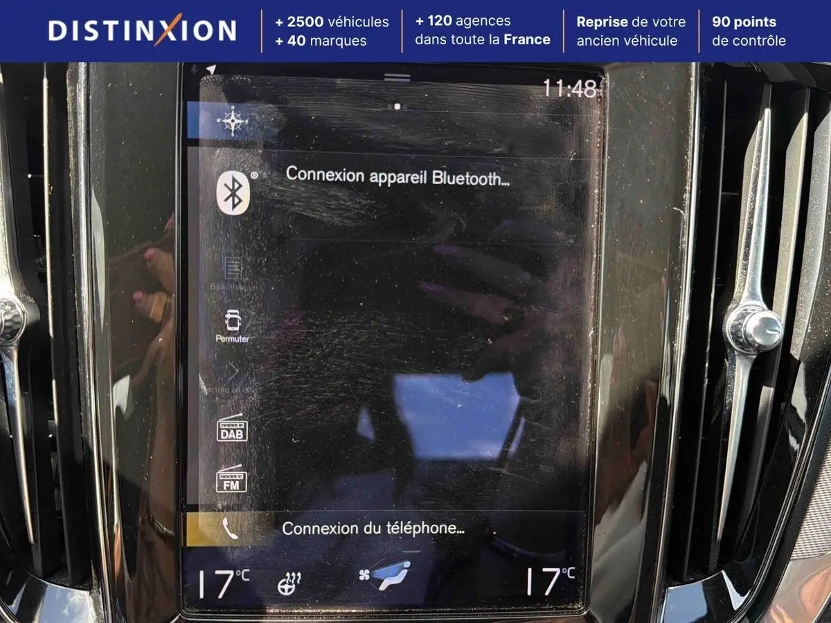 Écran tactile central du tableau de bord du Volvo S60 T8 blanc, avec commandes de climatisation et connectivité Bluetooth visibles.