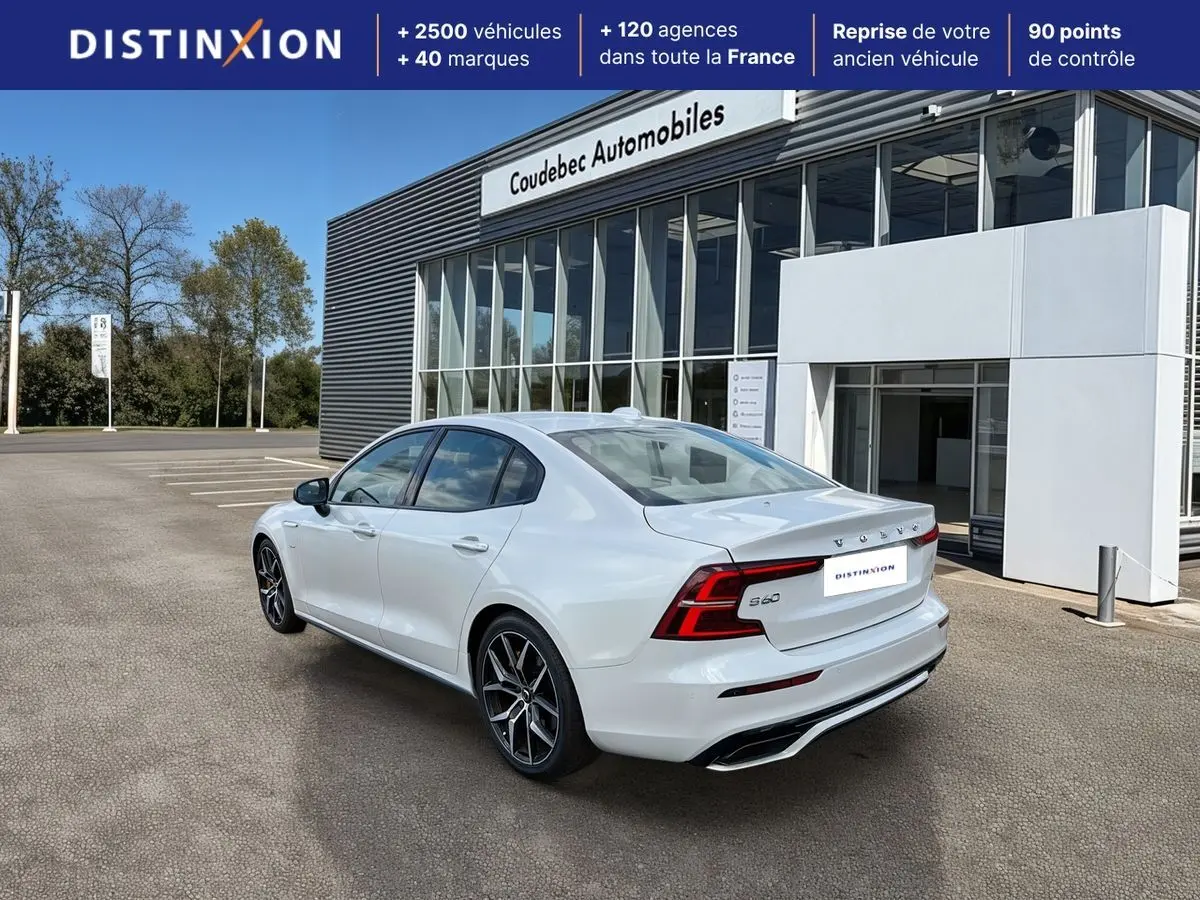 Vue 3/4 arrière droite d'une Volvo S60 blanche avec jantes alliage noir et calandre noire brillante devant un bâtiment commercial.