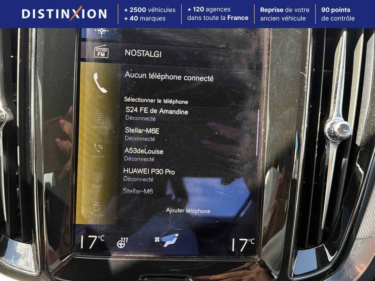 Vue rapprochée de l’écran tactile central noir de la Volvo S60 blanche, affichant la connexion Bluetooth et la température à 17°C.