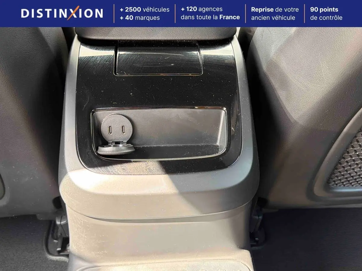 Prise USB et console centrale en plastique noir mat dans l'habitacle arrière d'une Volvo S60 blanche.