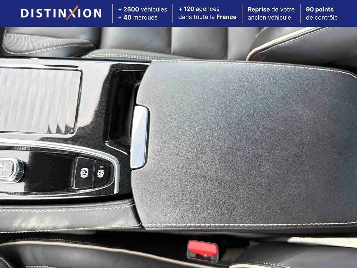 Gros plan sur la console centrale en cuir noir avec surpiqûres beige et commandes électroniques d'une Volvo S60 blanche.