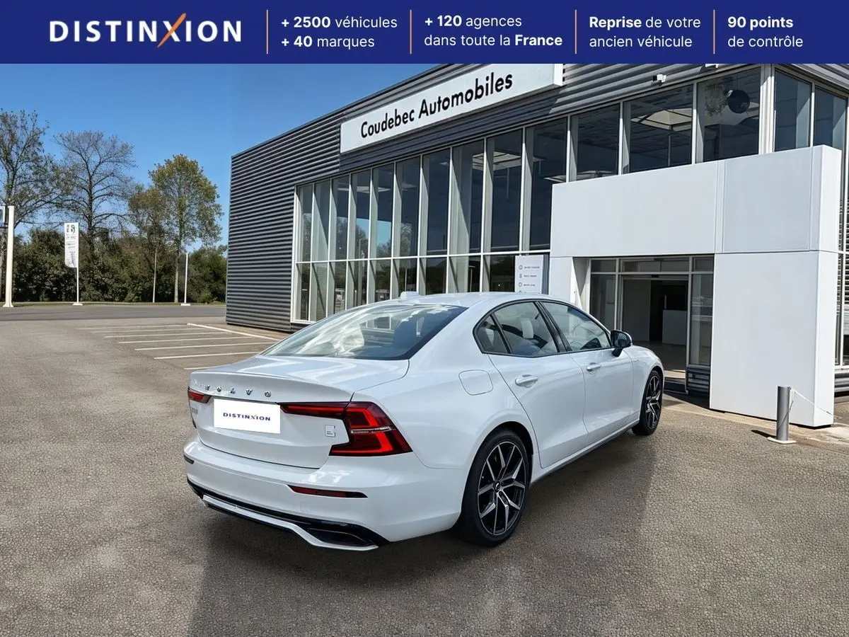 Vue 3/4 arrière droite d'une Volvo S60 T8 blanche avec jantes noires et calandre brillante, devant un showroom.