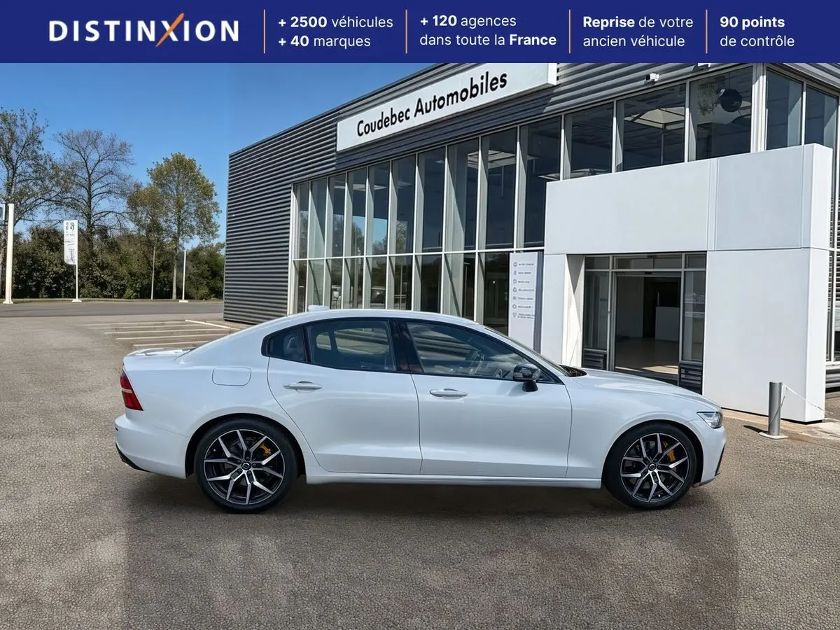 Profil droit d'une Volvo S60 T8 Twin Engine blanche avec jantes 19 pouces style Y noir et freins dorés, devant un bâtiment.