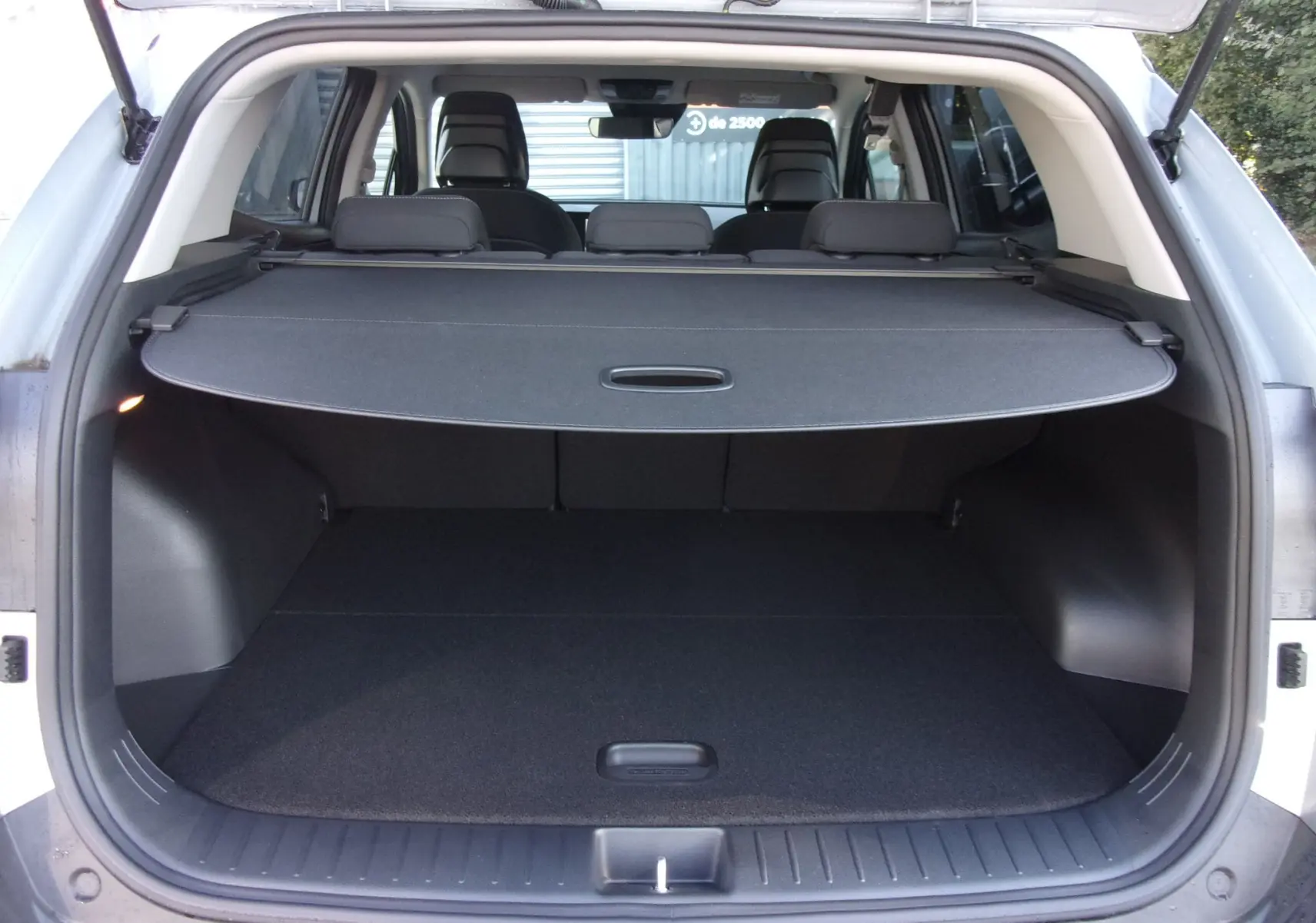 Coffre ouvert du KIA SPORTAGE gris perle vu de l'arrière, avec cache-bagages déployé et sièges arrière visibles.
