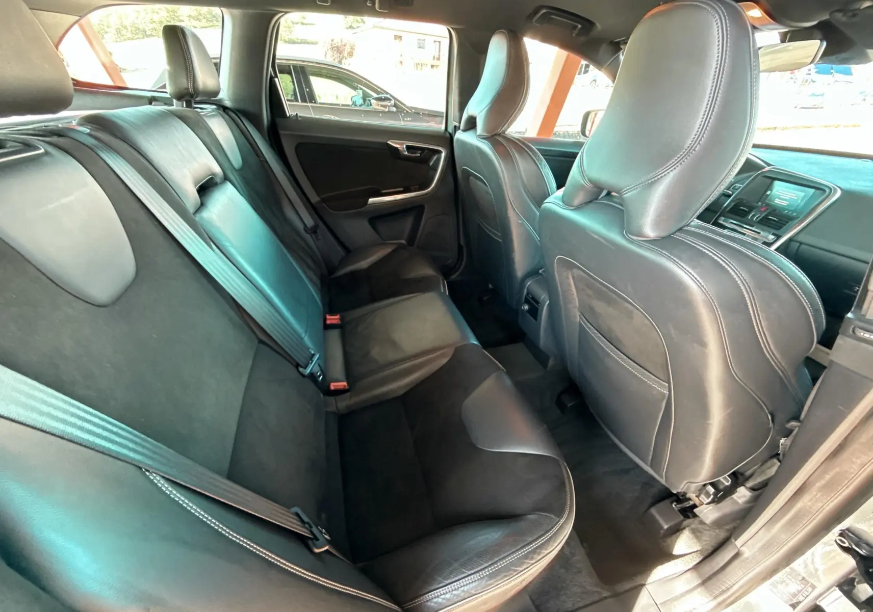 Vue intérieure arrière du Volvo XC60 gris 2016, montrant les sièges en cuir noir et les ceintures de sécurité.