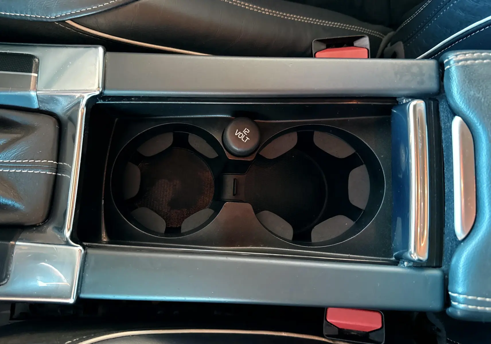 Vue rapprochée de la console centrale grise du Volvo XC60 2016 montrant les porte-gobelets et prise 12 volts.