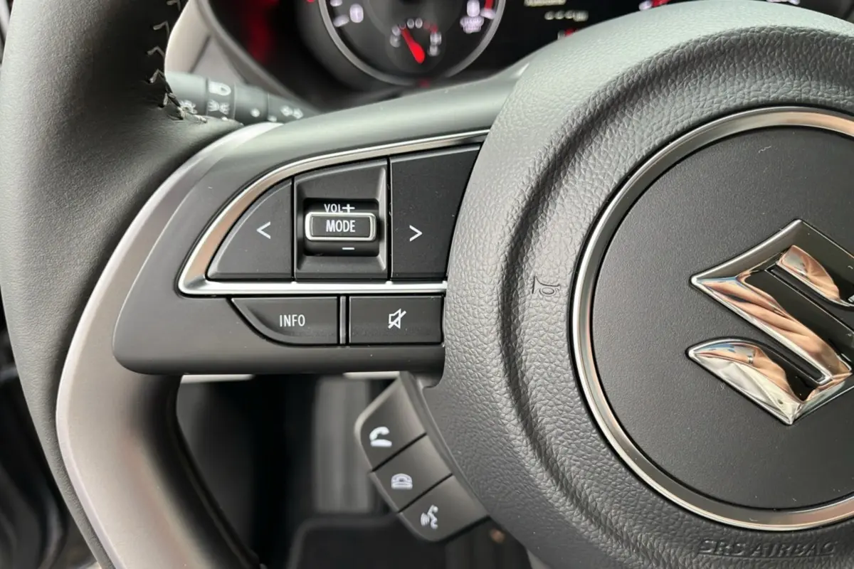 Gros plan sur le volant cuir multifonctions de la Suzuki Swift 2025, avec commandes audio et logo Suzuki central.