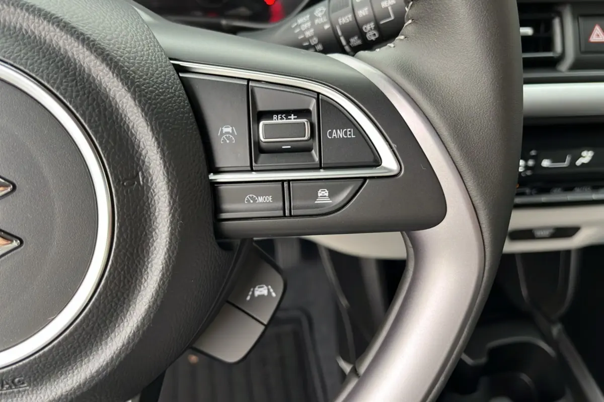 Gros plan sur le volant cuir multifonctions de la Suzuki Swift 2025, mettant en avant les commandes de régulateur de vitesse.