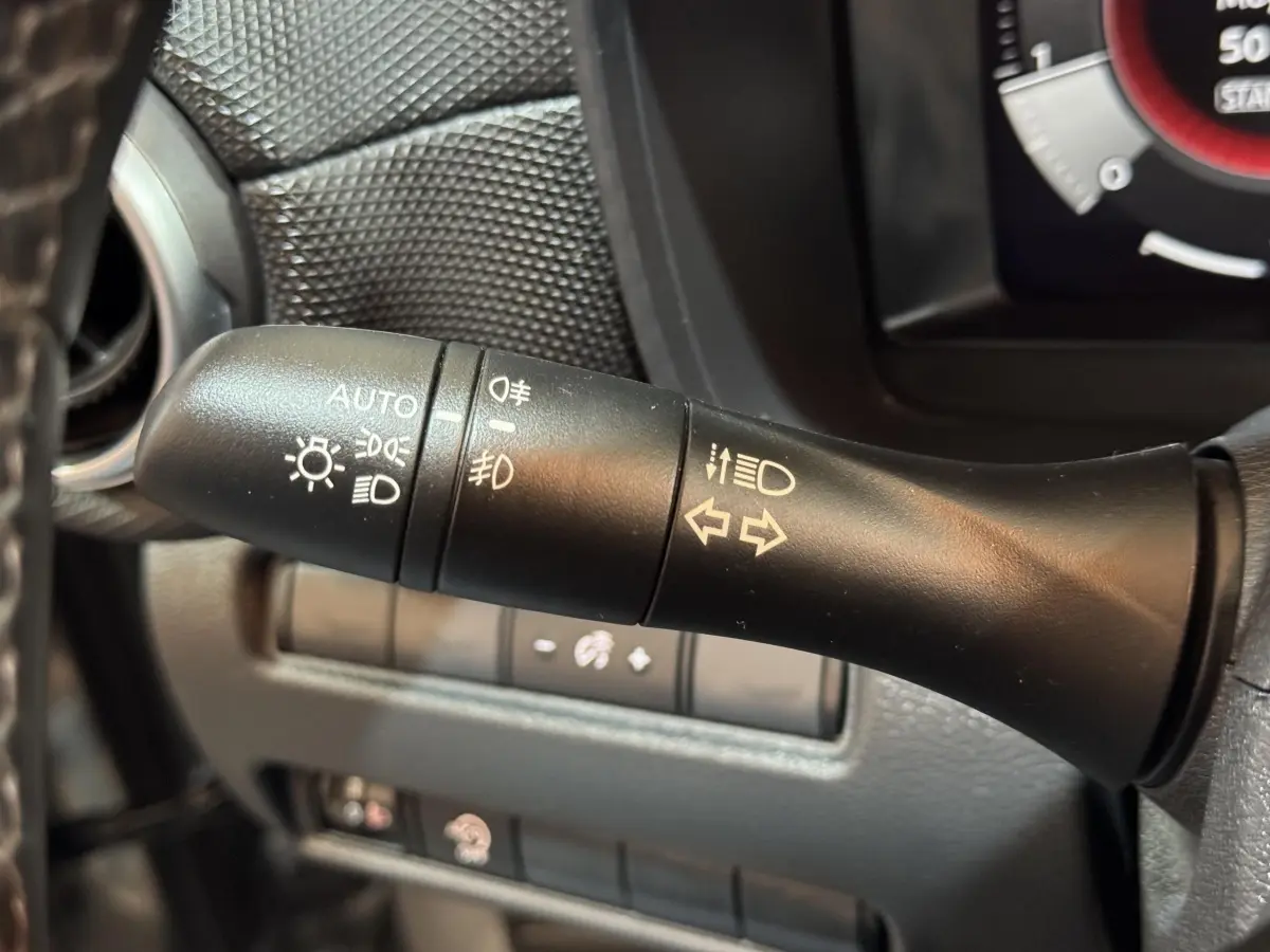 Gros plan sur la commande des feux et clignotants côté gauche du volant dans un Nissan Juke gris clair 2025.