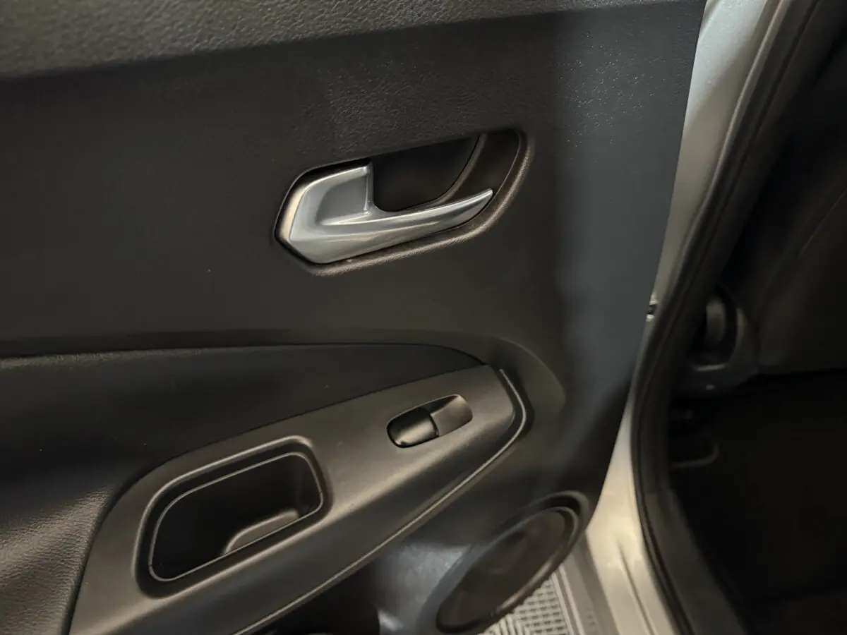 Poignée intérieure et commande de vitre sur la porte arrière droite d'un Nissan Juke gris clair, vue rapprochée.