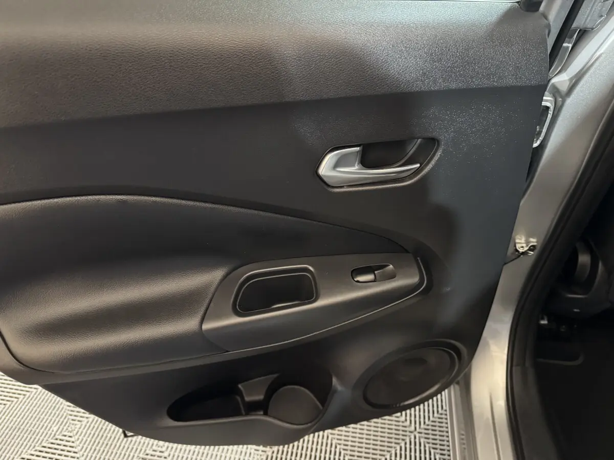 Vue rapprochée de la porte intérieure côté droit du Nissan Juke gris clair, avec poignée argentée et haut-parleur intégré.