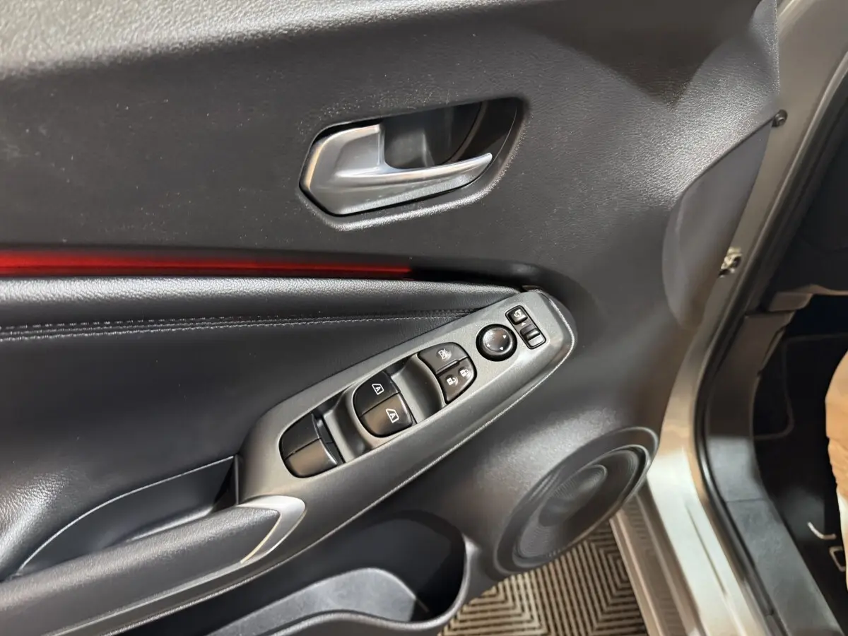 Vue rapprochée de la porte avant gauche gris clair du Nissan Juke 2025 avec commandes de vitres et poignée alu.