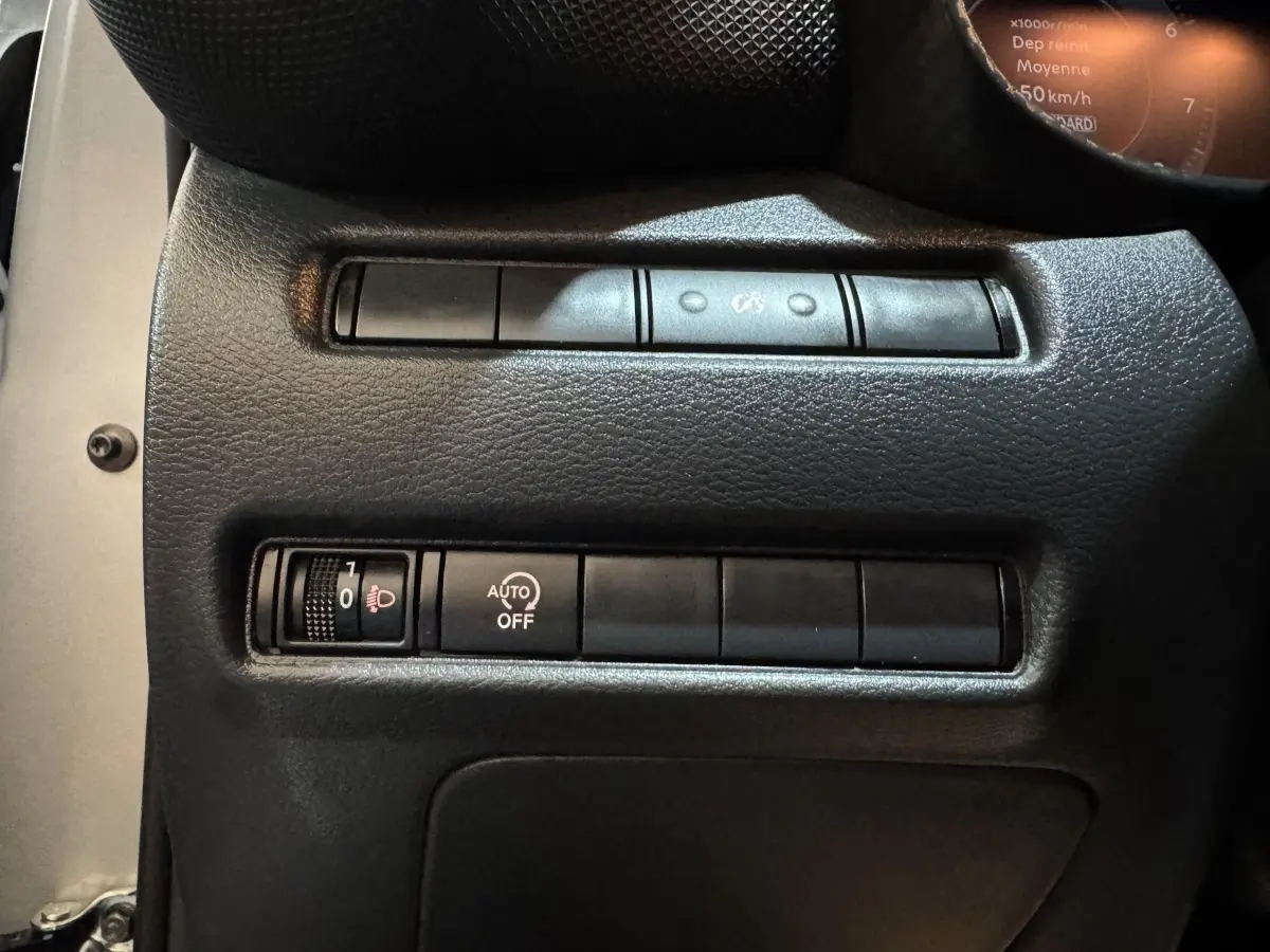 Gros plan sur les commandes de réglage des phares et d'activation automatique dans un Nissan Juke gris clair 2025.