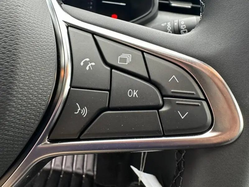 Gros plan sur les commandes multifonctions au volant côté gauche d'une Renault Clio gris 2025, boutons noirs avec cadre argenté.