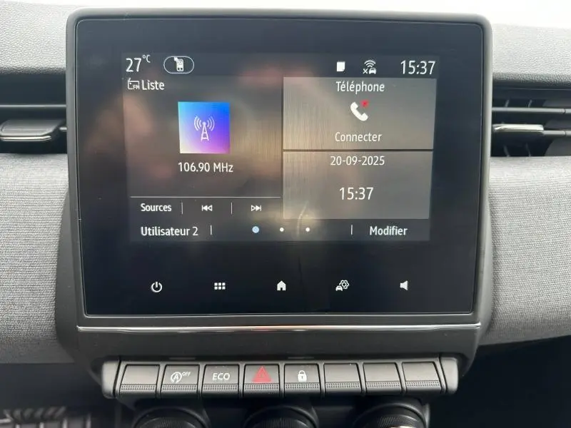 Écran tactile central de la Renault Clio gris 2025 affichant radio et options téléphone, avec boutons de commande en dessous.