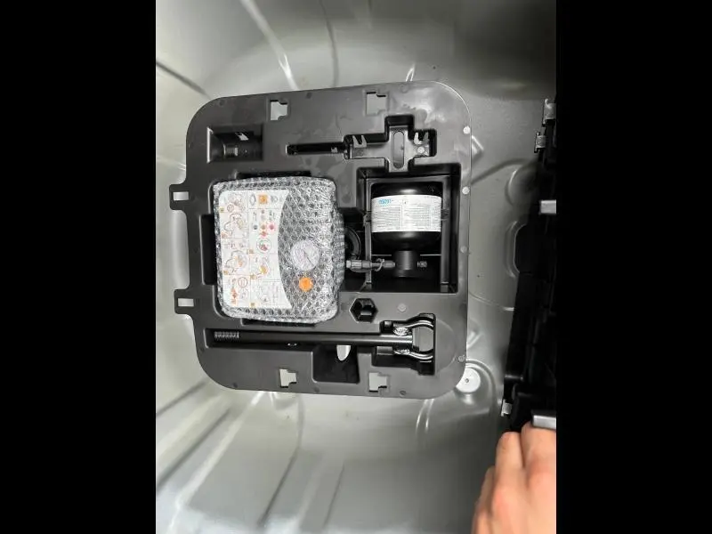 Vue plongeante sur le coffre d'une Renault Clio 2025 gris, montrant le kit de réparation pneu et outils rangés.