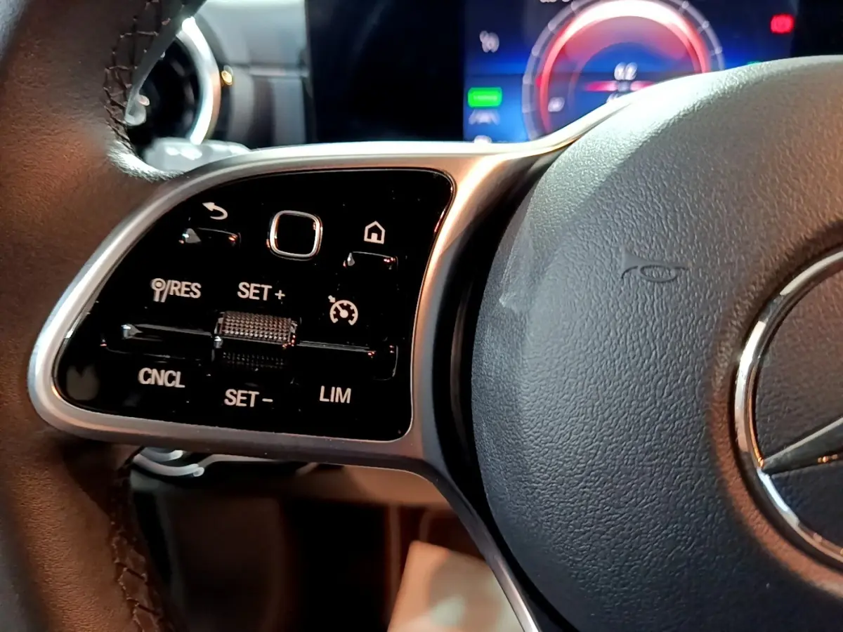 Gros plan sur le volant noir de la Mercedes Classe A 250 e, avec commandes multifonctions et affichage numérique en arrière-plan.