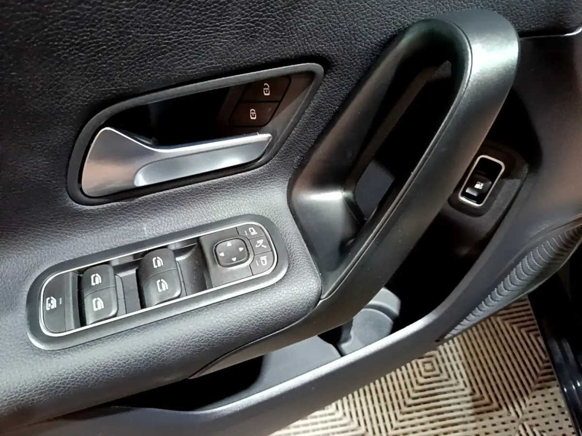 Gros plan sur la porte avant gauche noire de la Mercedes Classe A 250 e avec commandes de vitres et poignée intérieure.
