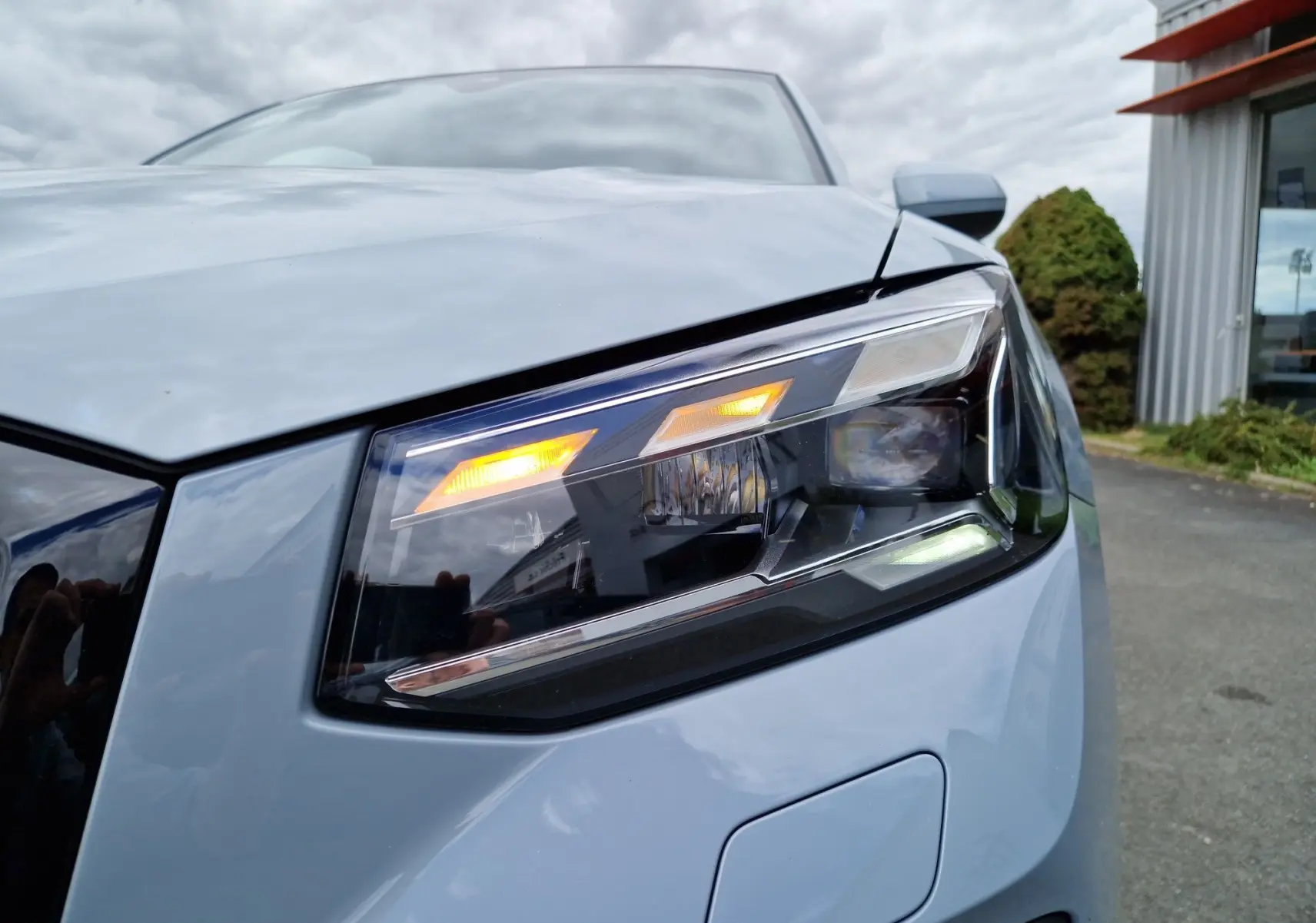 Gros plan sur le phare avant droit allumé de l'Audi Q2 35 TFSI gris flèche, finition S line 2023.