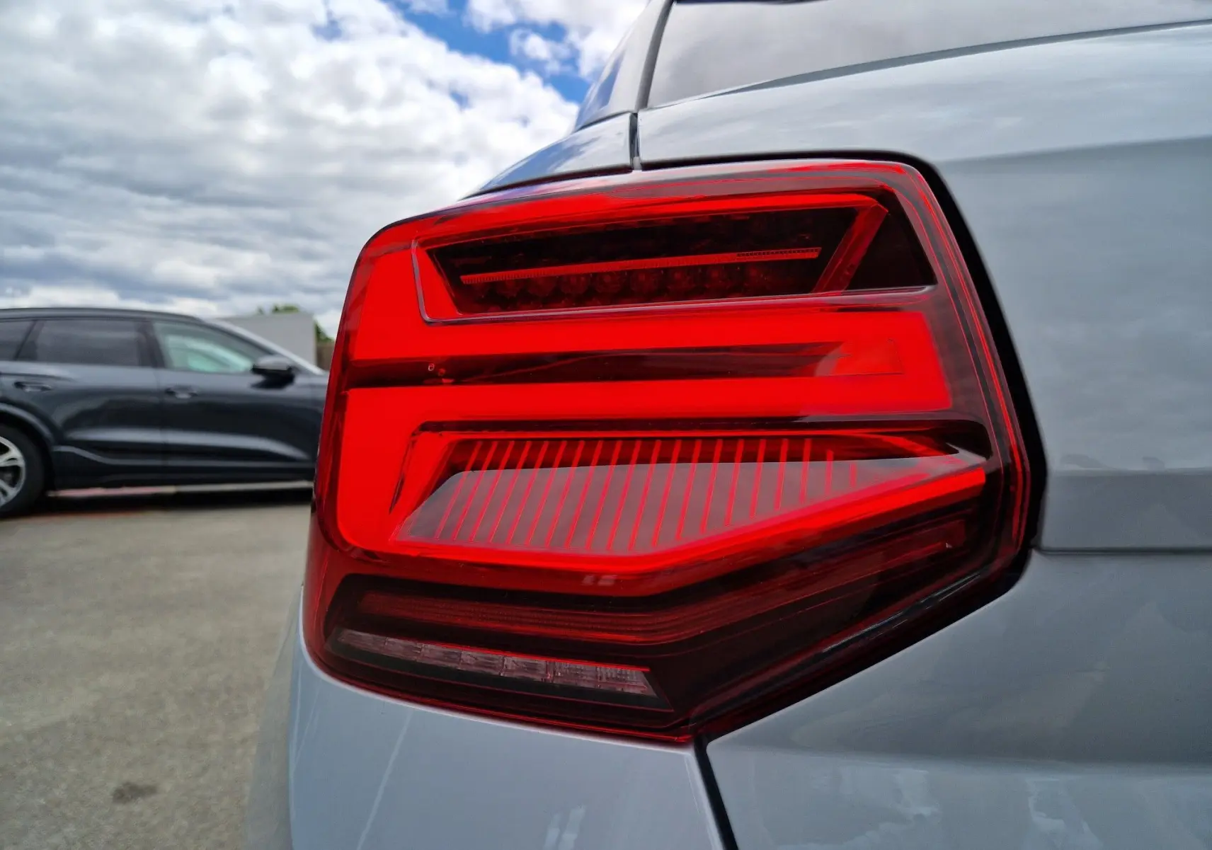 Gros plan sur le feu arrière droit rouge vif de l'Audi Q2 35 TFSI 2023 en gris flèche, soulignant la finition S line.