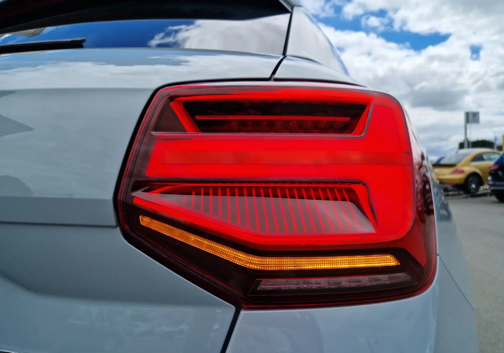 Gros plan sur le feu arrière droit rouge vif d’un Audi Q2 35 TFSI gris flèche 2023, avec carrosserie lisse et ciel en arrière-plan.