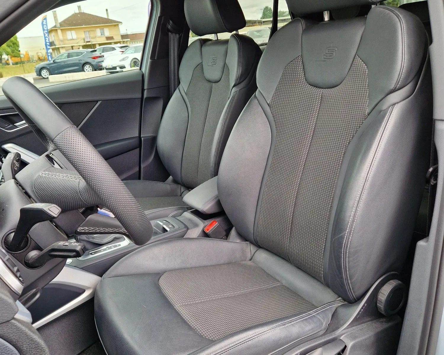 Vue intérieure côté conducteur de l'Audi Q2 35 TFSI 2023 gris flèche, sièges sport S line en cuir noir avec logo S embossé.