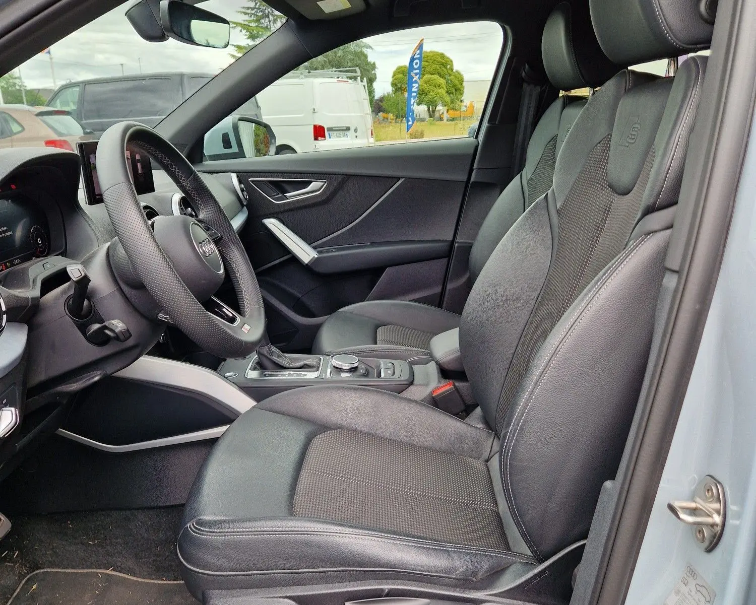 Vue intérieure côté conducteur de l'Audi Q2 35 TFSI 2023 gris flèche, sièges S line en cuir noir avec détails aluminium brossé.