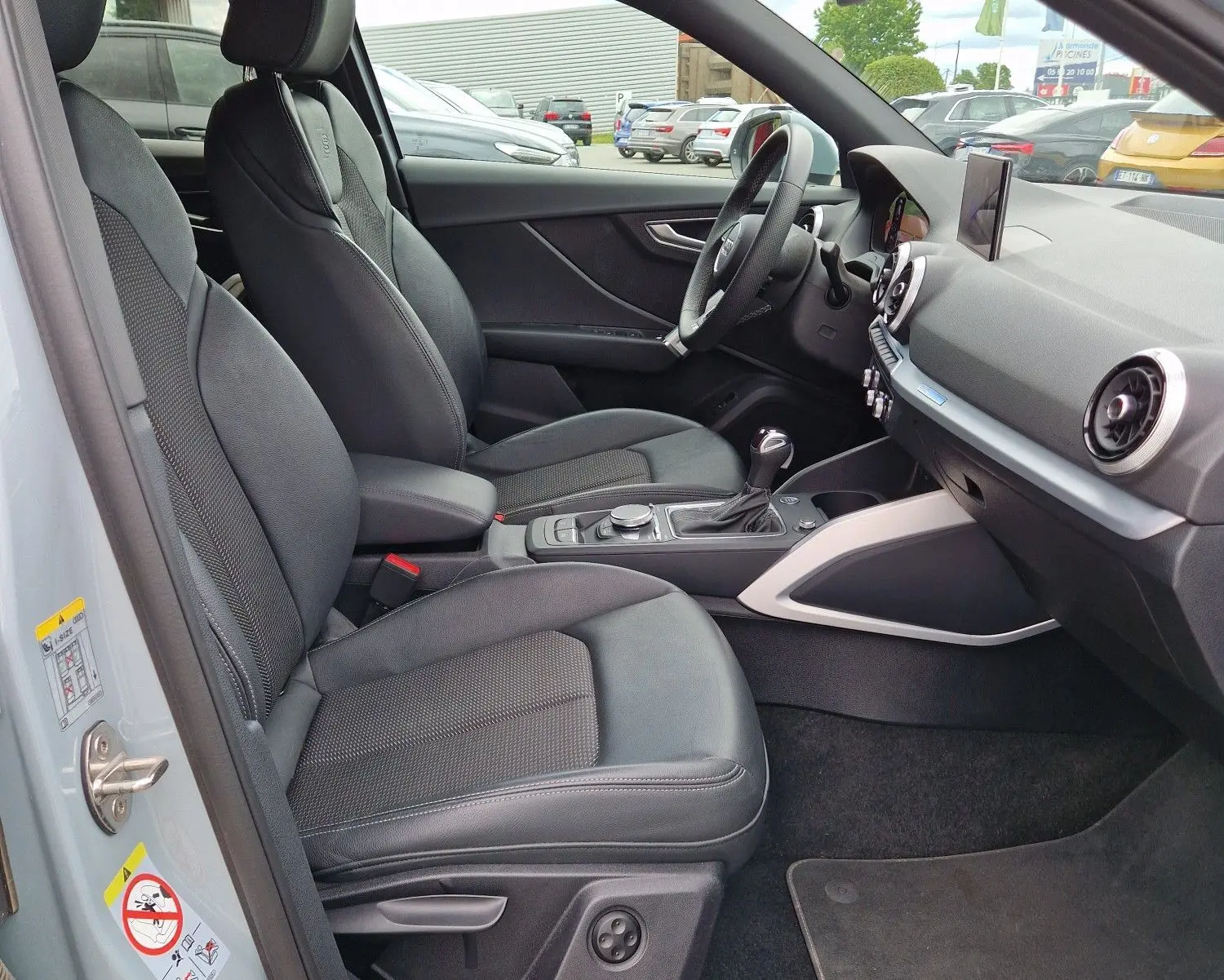 Vue intérieure côté conducteur de l'Audi Q2 2023 gris flèche, avec sièges sport S line en cuir et tableau de bord moderne.