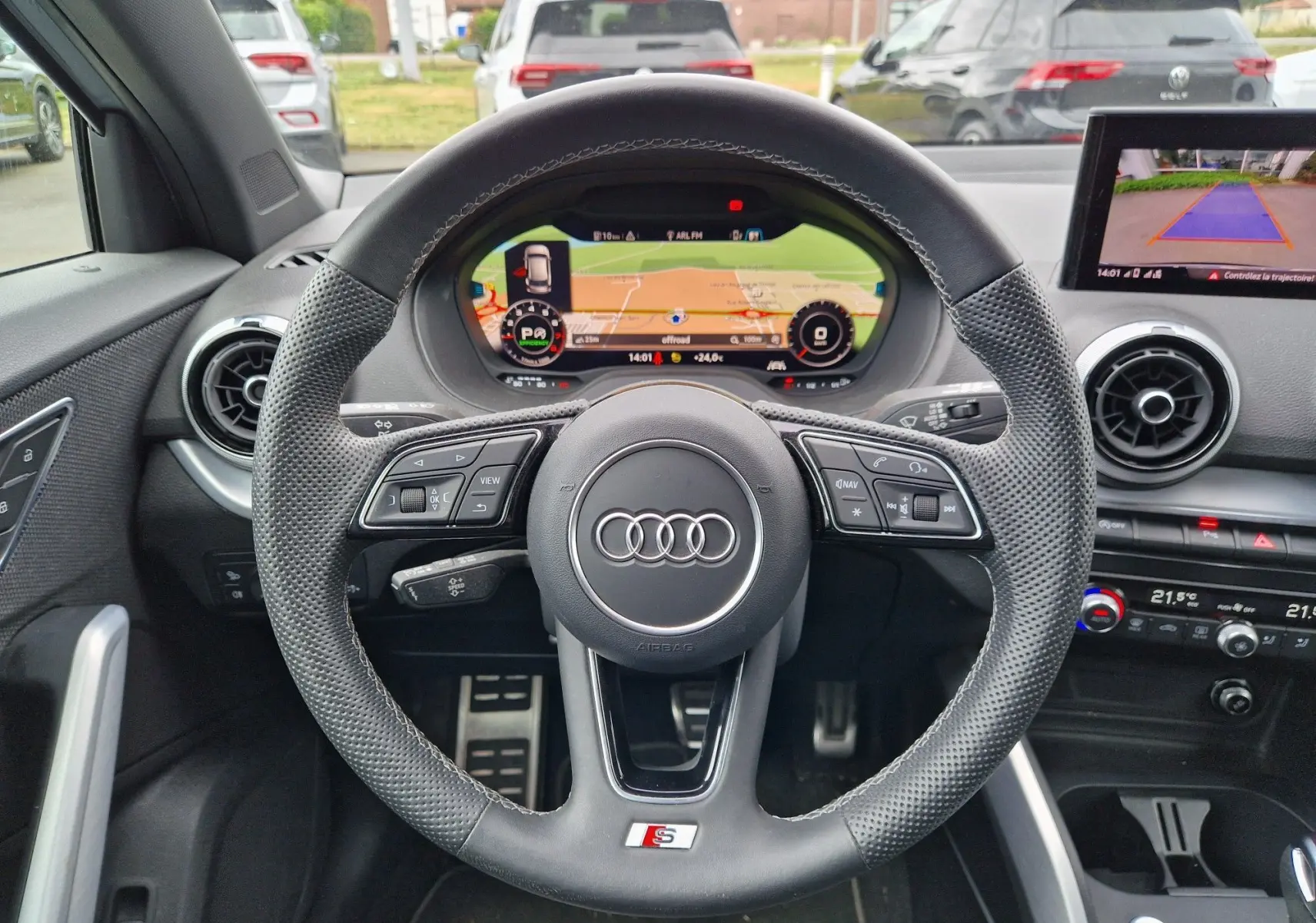 Vue intérieure centrée sur le volant S line et l'Audi virtual cockpit du Q2 gris flèche avec écran de navigation et caméra de recul.