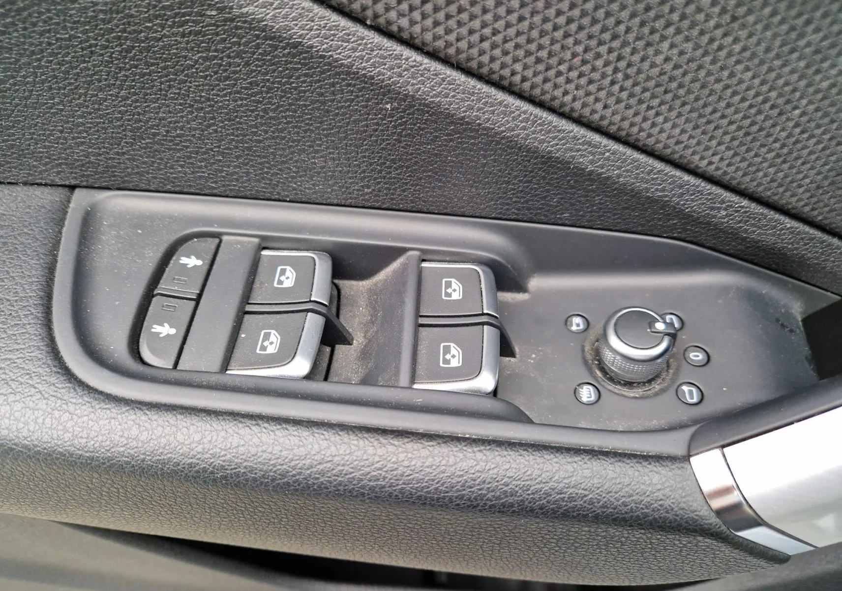 Gros plan sur les commandes de lève-vitres et réglage des rétroviseurs côté conducteur de l’Audi Q2 gris flèche.