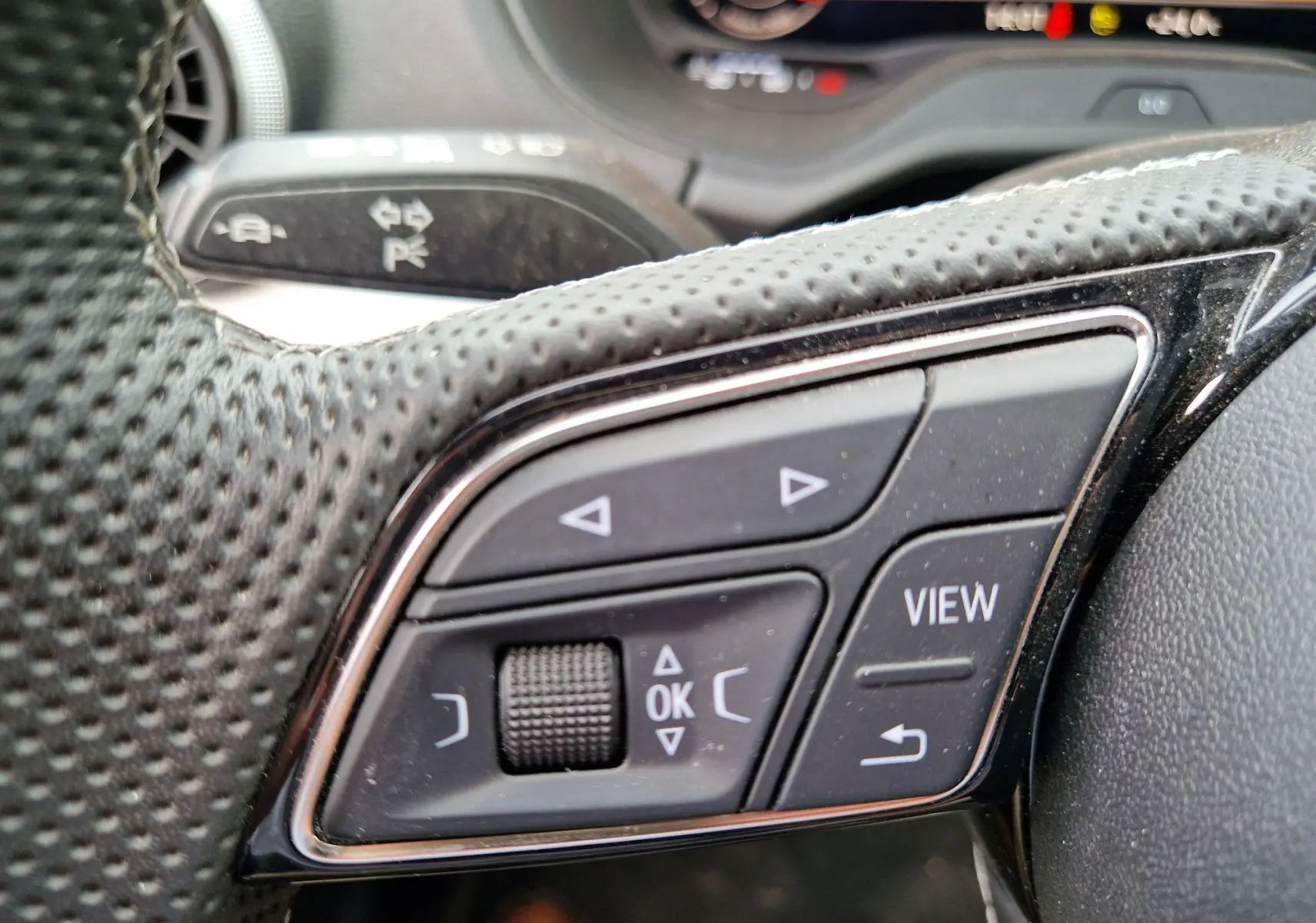 Gros plan sur les commandes multifonctions au volant perforé de l’Audi Q2 35 TFSI S line 2023, avec affichage digital en arrière-plan.